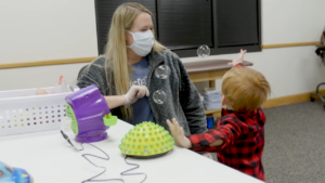 Child playing with adapted bubble maker, trying to catch bubbles